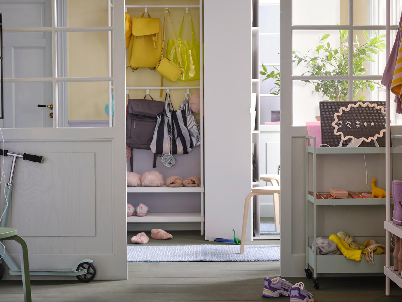 Helles, buntes Vorzimmer mit einem VIHALS Kleiderschrank neben einem MACKAPÄR Garderobenständer, an dem bunte Taschen und Schuhe zu sehen sind.