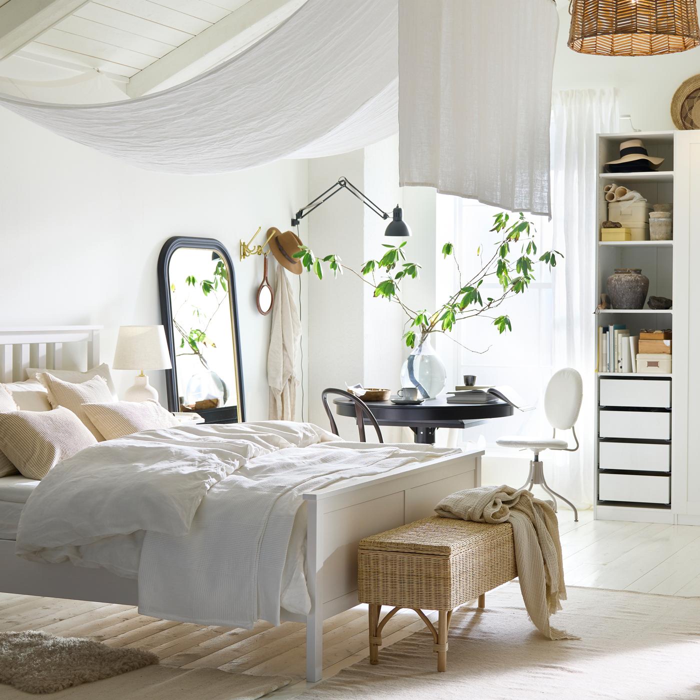 מיטה זוגית HEMNES בצבע לבן בחדר שינה לבן, בהיר ואוורירי עם שולחן נפתח INGATORP בצבע שחור ליד החלון מאחור.