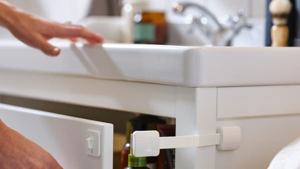 יד מחזיקה מגירה פתוחה בארון לכיור HEMNES בצבע לבן, שאליה מחובר מנעול UNDVIKA לבן.