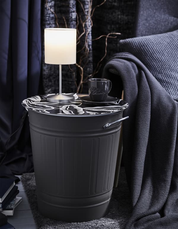 Hier dient eine KNODD Tonne als dekorativer Tabletttisch, auf dem eine Leuchte und eine Tasse Tee zu sehen sind.
