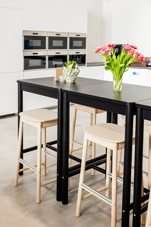 High black dining table with wooden stools and fresh tulip bouquet in office kitchen.