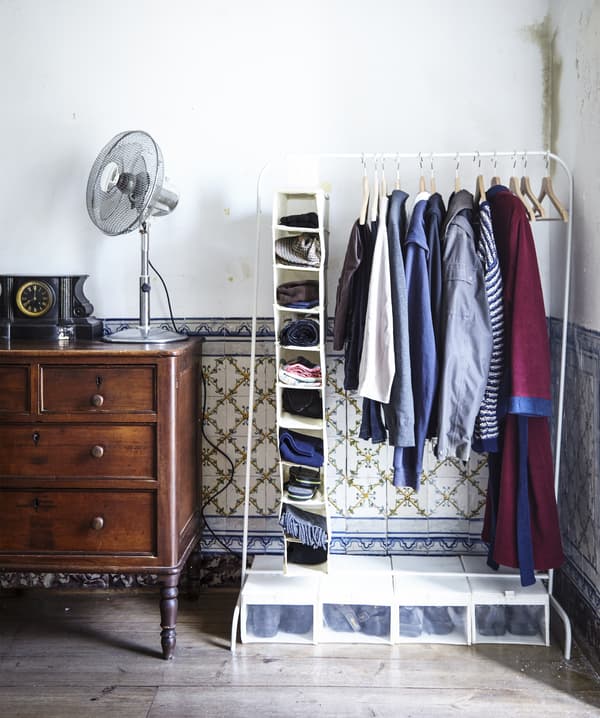 Historic wall tiles can be seen through the clothes hanging from a free-standing rail in this bedroom.