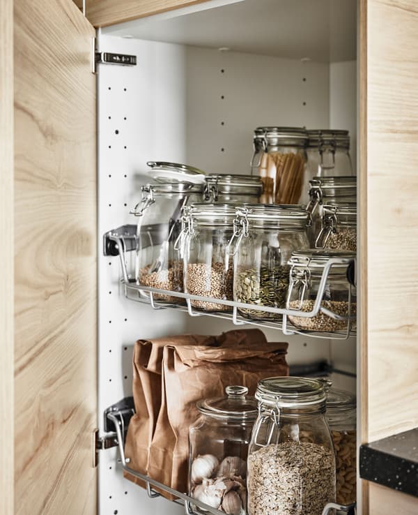 Hochschrank mit Eschentür, darin zu sehen sind Drahtkörbe mit KORKEN Dosen mit Deckel aus Klarglas.