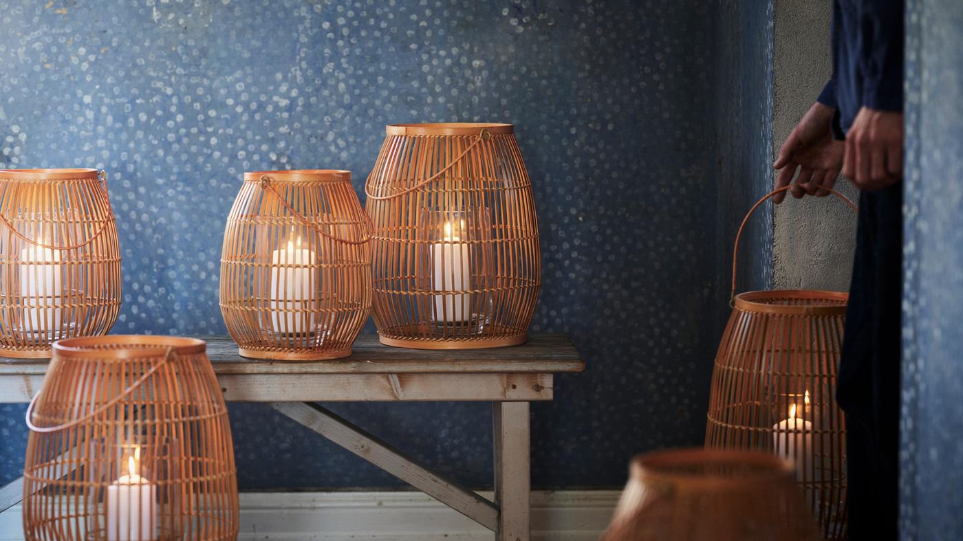 HÖVISK lanterns for block candles with lit candles inside them sit on and around a bench which stands against a wall.