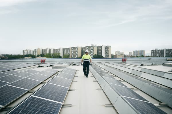 Hombre vestido con elementos de construccion caminando entre medio de paneles solares en una ciudad con cielo despejado.