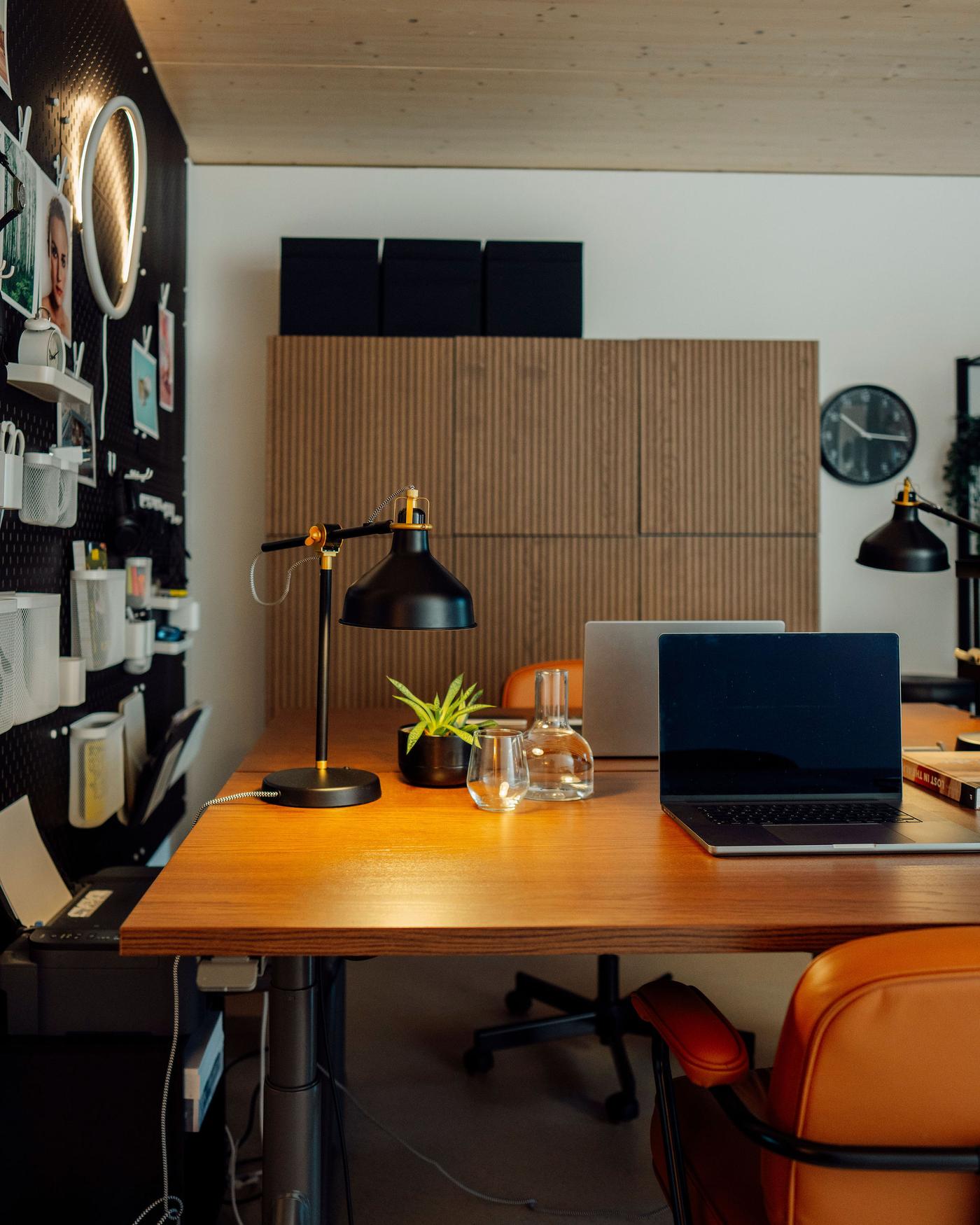 Home office con scrivania in legno, laptop, lampade, pianta e contenitori a parete e sul fondo.