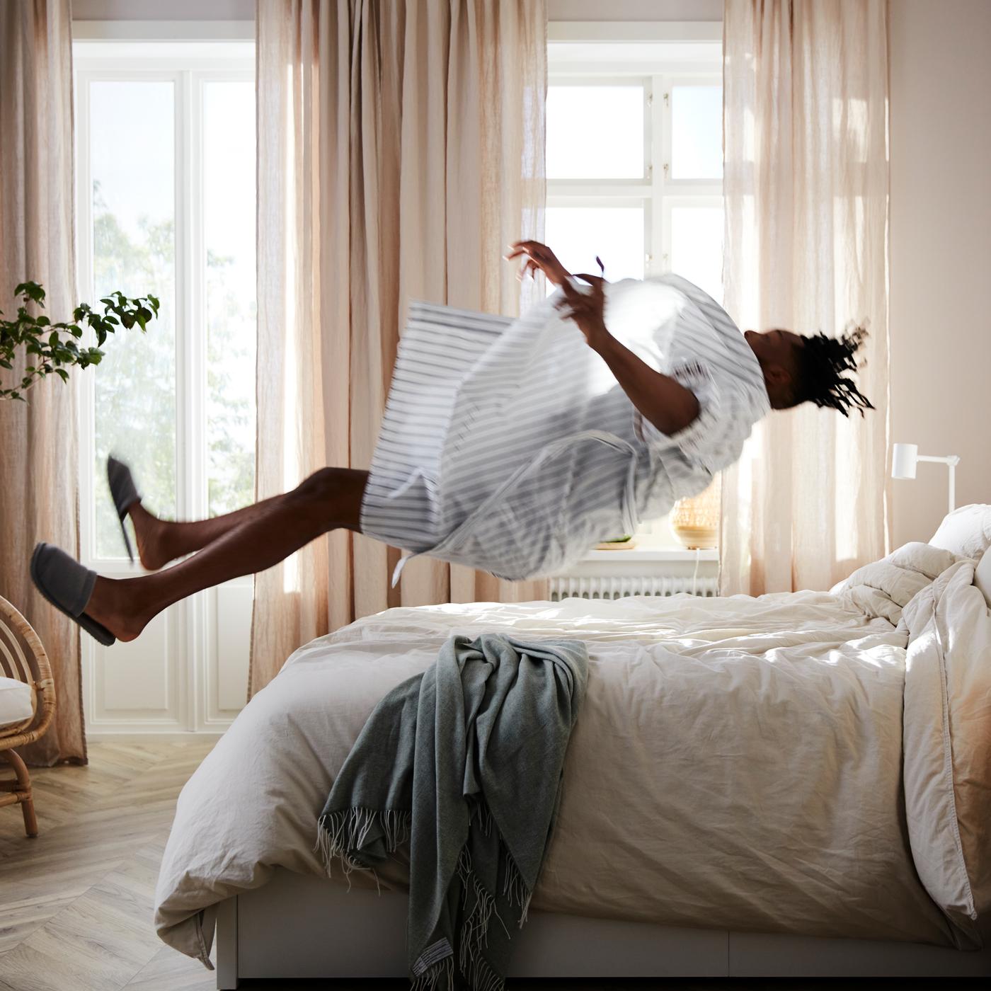 Homme se jetant en arrière sur un lit MALM avec matelas à ressorts ensachés VATNESTRÖM et linge de lit blanc.