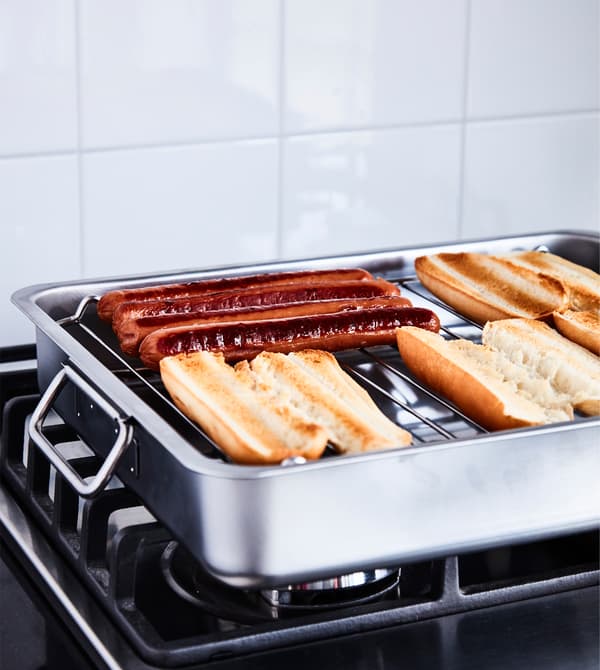 Hot dogs et petits pains posés sur une grille, sur une cuisinière.