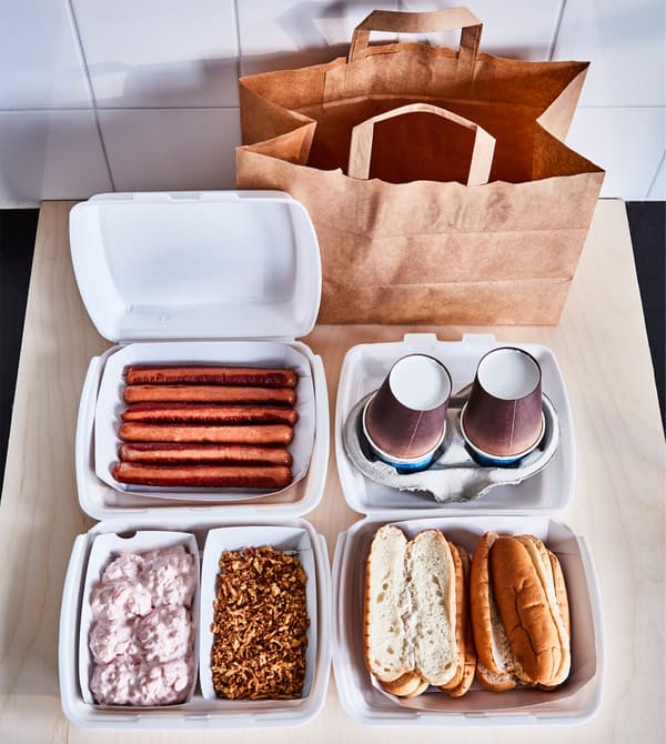 Hot dogs, petits pains, garnitures et gobelets, posés sur un plan de travail.