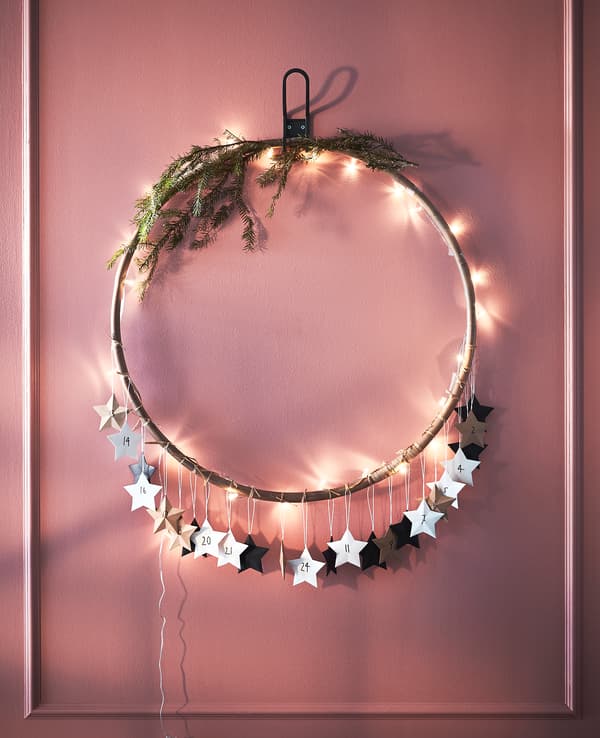 Hula hoop décoré de lumières, de verdure et d'étoiles en papier, accroché au mur.