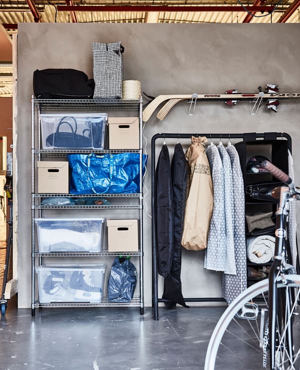 I vestiti e gli accessori invernali sono organizzati in scatole di cartone e plastica, robuste borse blu e appesi a uno stand appendiabiti in un garage - IKEA.