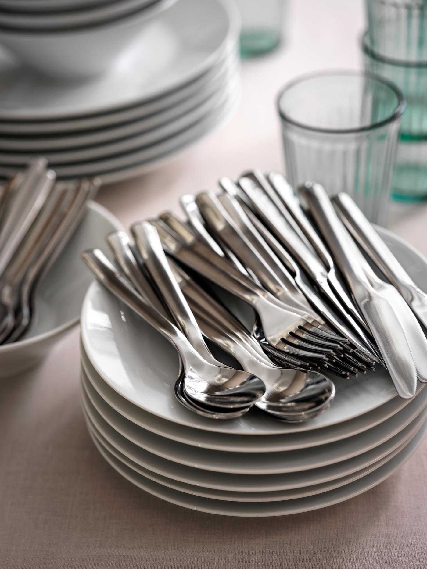 ערמת צלחות, כוסות וסכו"ם מקולקציית IKEA 365+ מונחים על משטח עליון לשולחן עם מפה ורודה.