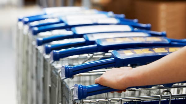 IKEA co-workers drive a row of trolleys through an IKEA store.