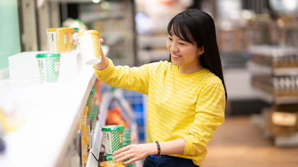IKEA coworker in a yellow striped top arranging colorful takeaway cups on a counter in a bright, busy store environment