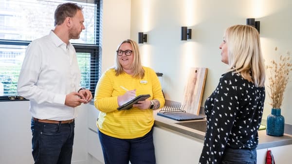 IKEA coworker is writing in a notebook while assisting two customers 
