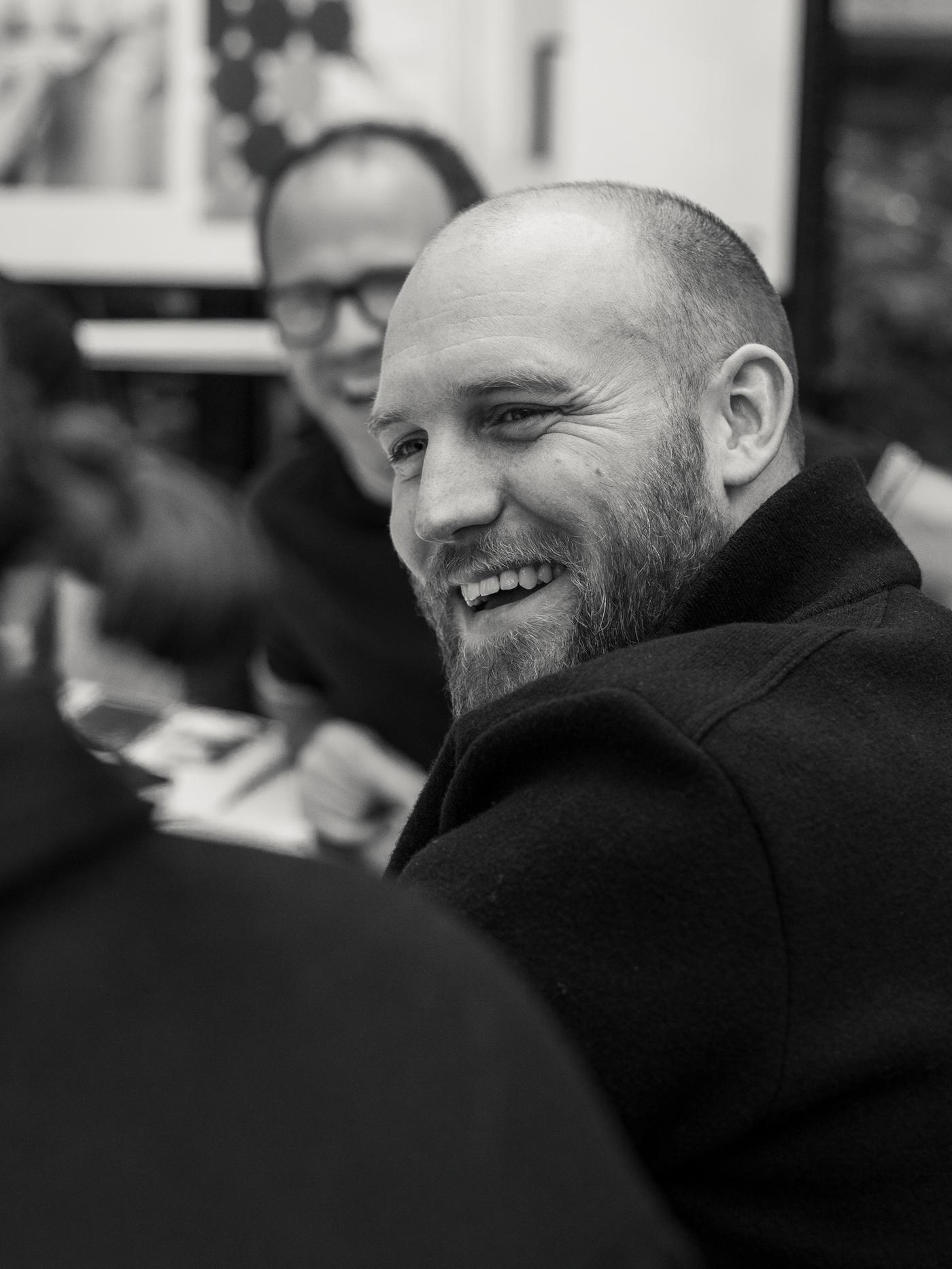 IKEA designer Friso Wiersma wearing a black jacket and looking at someone and laughing at a table with other people laughing.