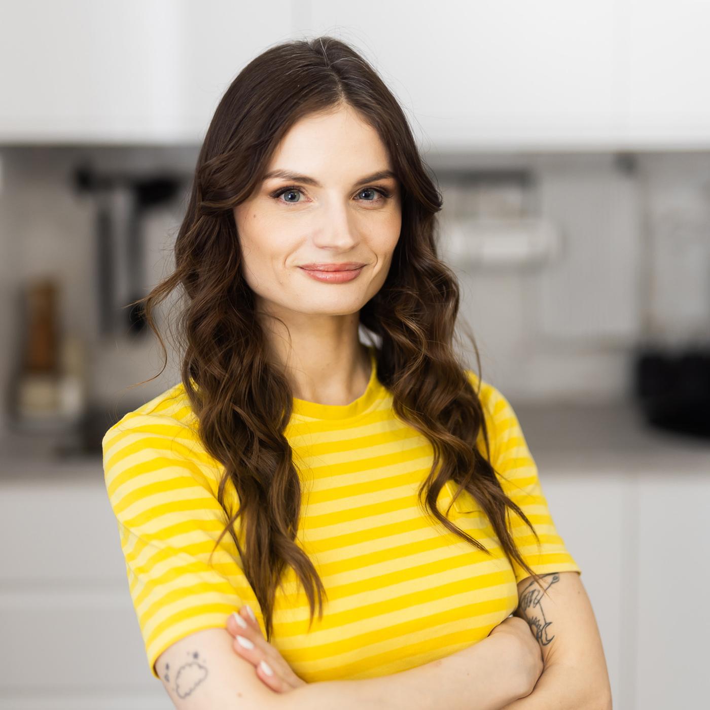 IKEA designer in a yellow uniform T shirt stands in a kitchen and smiles.