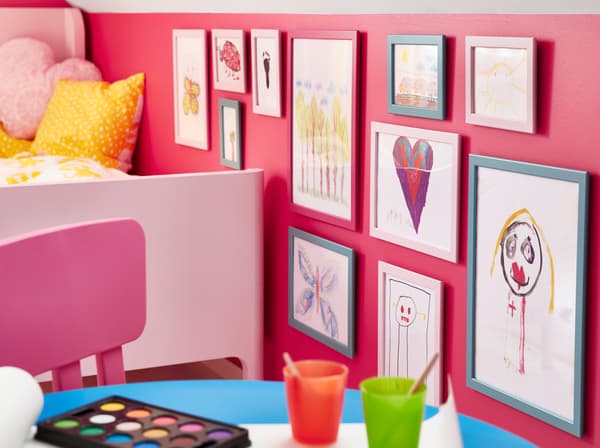 IKEA FISKBO fibreboard frames in blue and pink showcasing children's drawings.