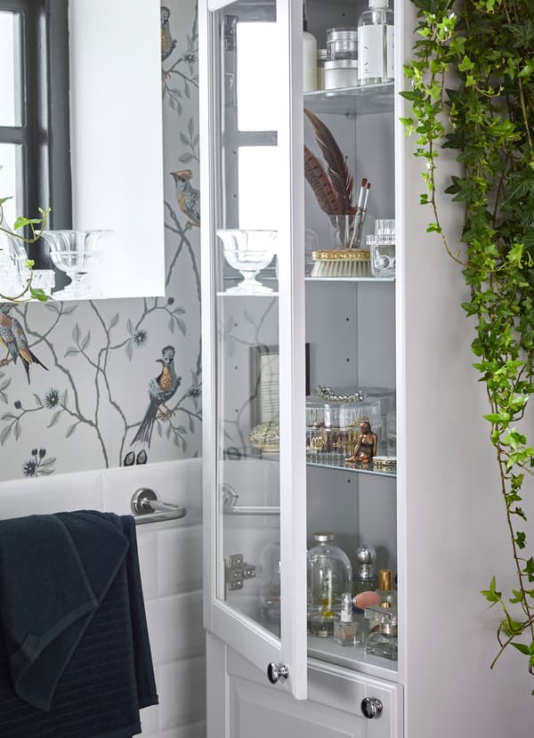 IKEA GODMORGON light grey high cabinet has closed storage doors on the bottom and clear glass doors on top and glass shelves inside to help display the things you love, while protecting them from moisture in the bathroom. SAMMANHANG clear glass boxes with cork tops are also a nice addition to store bathroom tools and jewelry.