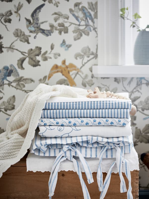 IKEA GULSPARV bed linen textiles folded in a pile on a wooden box in front of floral motif wallpaper.