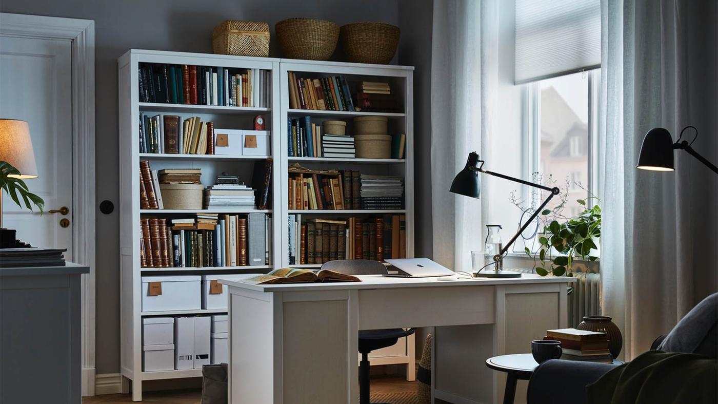 IKEA HEMNES desk in white in the middle of a bright room setting with a white bookcase at the back.