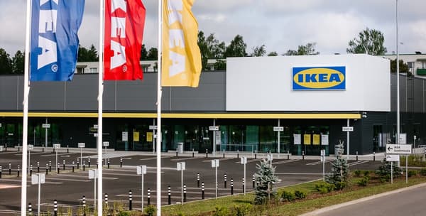 IKEA kaupluse välisvaade, mille ees on punased, kollased ja sinised IKEA lipud, enamasti tühi parkla ning eesti keeles olevad suunaviidad laadimisalale.
