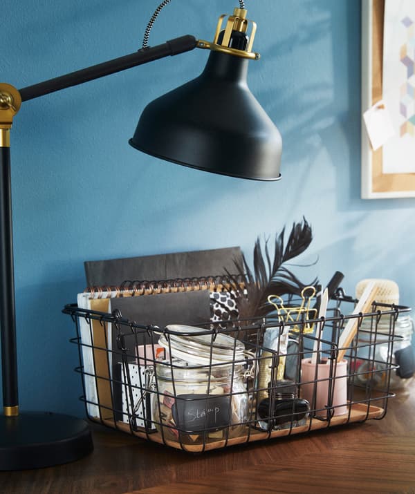 IKEA PLEJA wire basket beside a work lamp on a table.