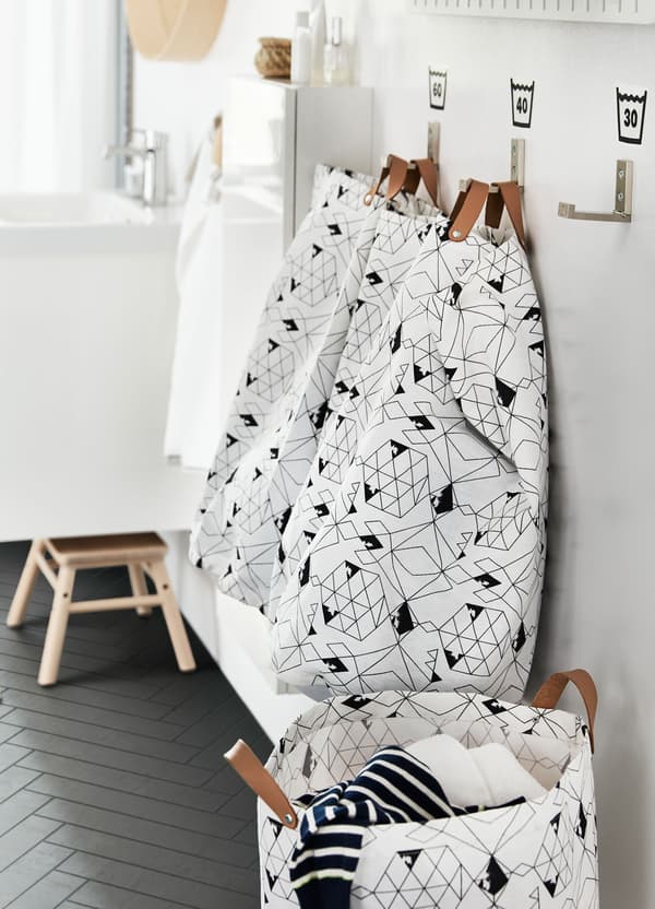 IKEA PLUMSA round laundry bag hampers, with leather straps and white and black geometric patterned fabric, on hooks.