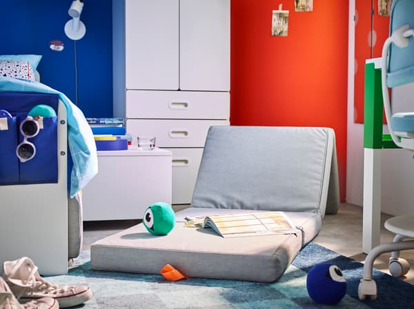 IKEA SLÄKT long light grey play mattress propped up as a seat in a children's bedroom.