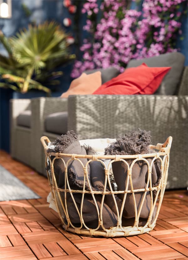 IKEA SNIDAD rattan basket holding textiles and blankets in an outdoor space.