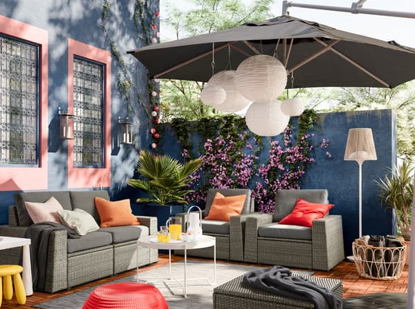 IKEA SOLLERÖN outdoor seating solution with removable dark grey covers in a colourful outdoor space with deep blue walls.