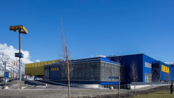 IKEA store in Innsbruck with yellow and blue facade in front of snow-covered mountains and clear blue sky.