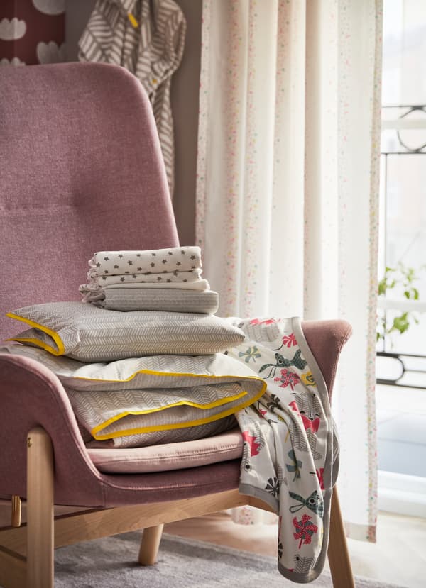 IKEA VEDBO pink chair holding baby bedsheets and blankets.