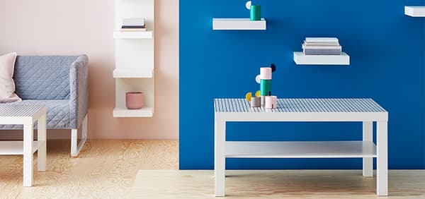 IKEA Wohnzimmer mit einer kleinen Couch sowie ein Beistelltisch und ein kleiner weißer TIsch vor einen blauen Mauer.