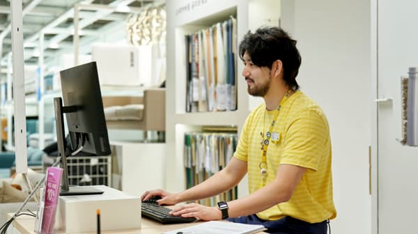 イケア店舗の売場カウンターで、コワーカーがデスクトップPCを使いながらお客さま対応やサービス業務を行っている様子。