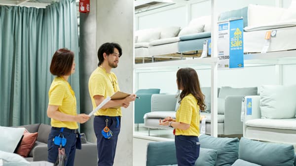 イケア店舗のショールームで、コワーカーがソファ売場のセールや展示について打ち合わせをしている様子。