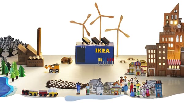 Illustrated IKEA scene with wind turbines, factory, store, trees, and small town buildings with people and vehicles.