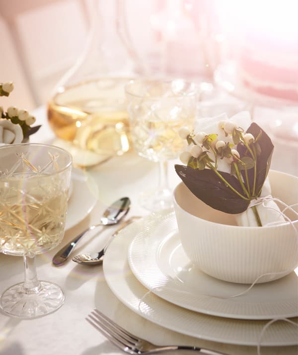 Image d’une place individuelle à table avec des verres, de la vaisselle et des décorations florales tout en blanc, créant ainsi une impression de luxe.