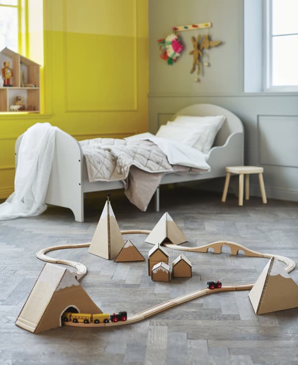 In a kids’ bedroom, a toy train set rides through a mountain range made of cardboard.