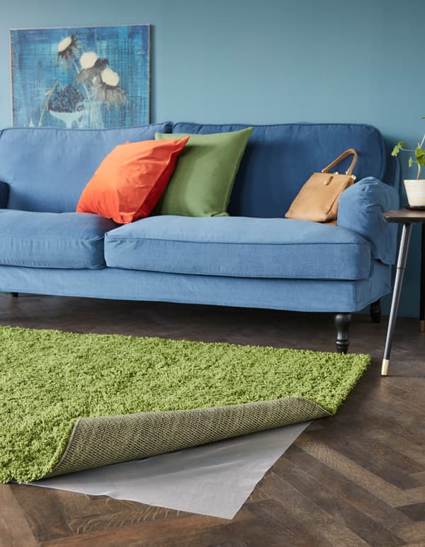 In a living room, a rug is rolled back to reveal an anti-slip underlay underneath.