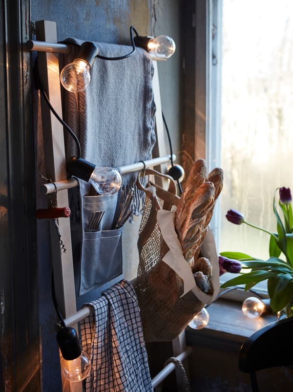 In a rustic room, a light chain decorates a towel stand that’s being used as a clever, space-saving storage solution.