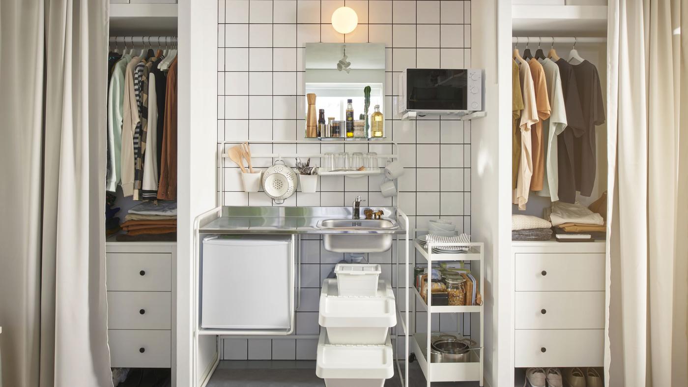 In a shared dorm room, a SUNNERSTA mini kitchen is sandwiched between two closets. Curtains hang in front of the closets.