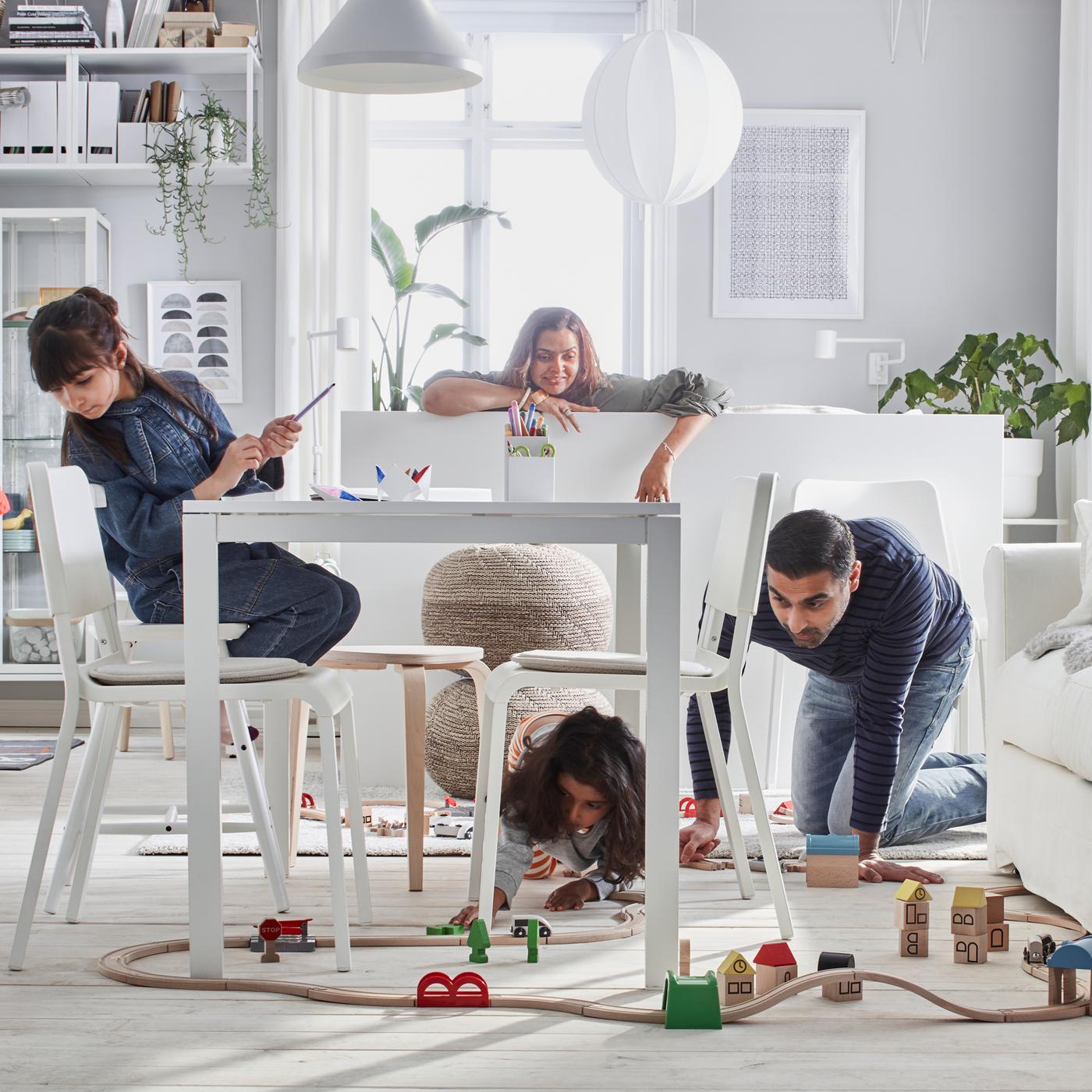 In einem weissen Wohnzimmer spielt eine vierköpfige Familie mit einem LILLABO Eisenbahn-Set mit Schienen.