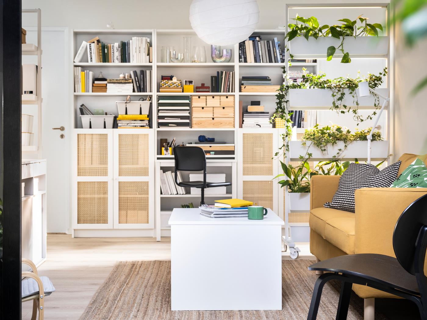 In einem Wohnzimmer stehen BILLY Bücherregale an einer Wand hinter einem MITTZON Gestell mit Rollen, einem verstellbaren ÖSTAVALL Couchtisch und einem Sofa.