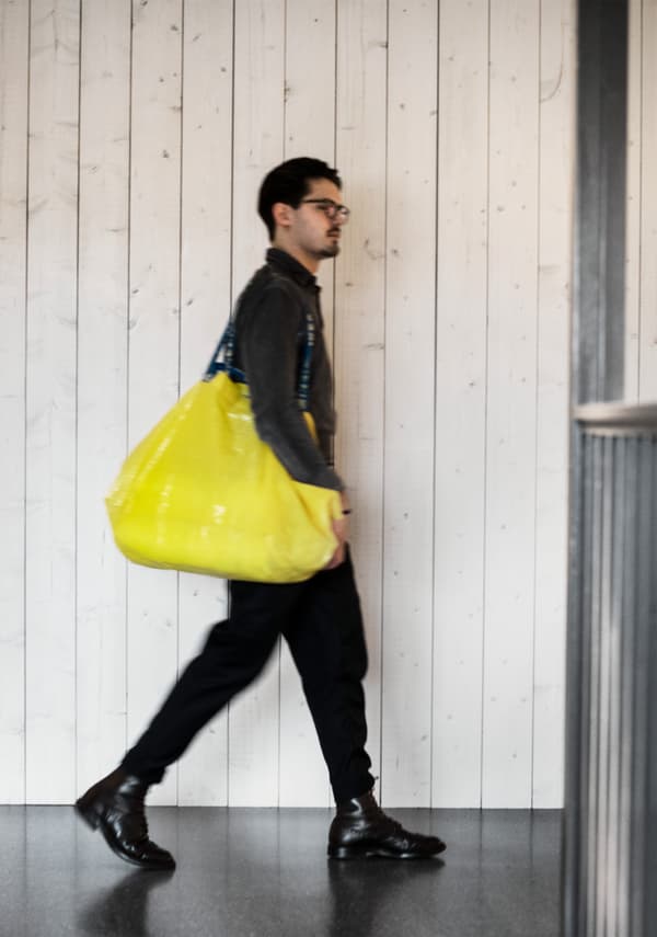 In het zwart geklede jongeman loopt door een IKEA winkel met een gele boodschappentas over zijn schouder.