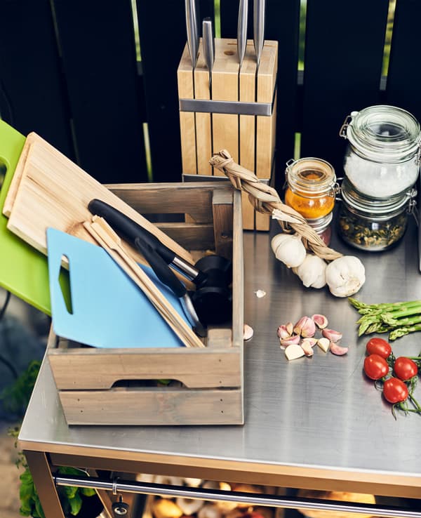 Ingrédients frais, boîte remplie d’ustensiles de cuisson et range-couteaux posés sur un plan de travail en acier inoxydable.