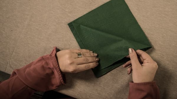 Instructions de bricolage, étape 1 : tourne une serviette de table carrée de manière à ce que les languettes soient tournées vers le haut, loin de toi. Replie chaque languette en laissant une marge d'environ 1 cm vers les bords.