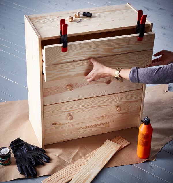 Interiérová designérka upevňuje pomocí svorek čelo na horní zásuvku komody IKEA RAST, které dodává nový vzhled.
