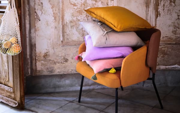 Intérieur épuré en matériaux bruts. Sur un fauteuil, une pile de coussins, dont un enveloppé dans une housse KLARAFINA.