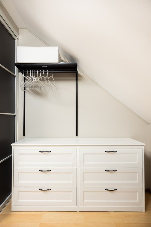 Interior view of a wardrobe with drawers, shelves, and hanging rails fitted under a sloped ceiling for efficient storage.